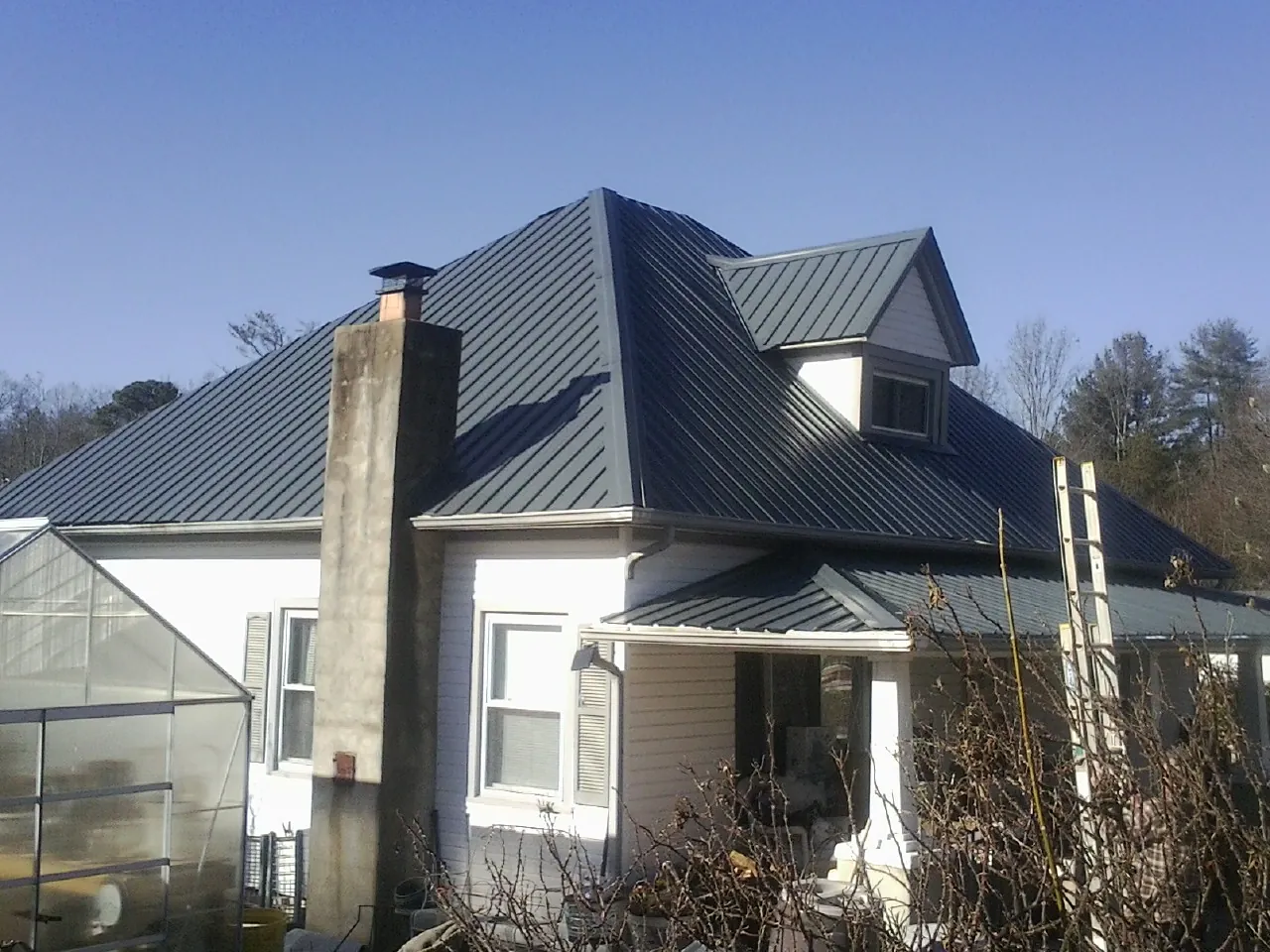 Dark blue standing seam metal roof on a white farmhouse with dormer — Slate & Tile Roof Repair by Roofing Brothers in Clearfield