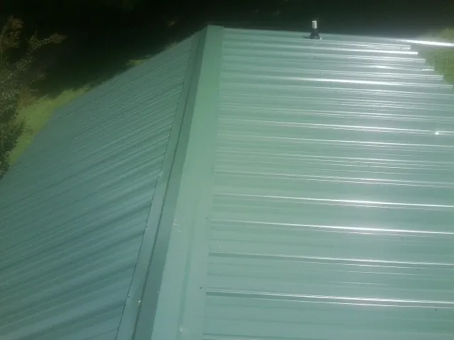 New green metal panels meeting at the ridge of a roof — Flat Roof Repair work by our crew in Clearfield